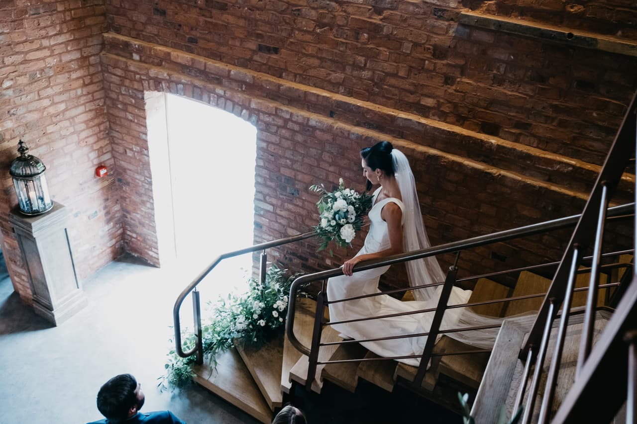 A bride walking downstairs holding her wedding bouquet.